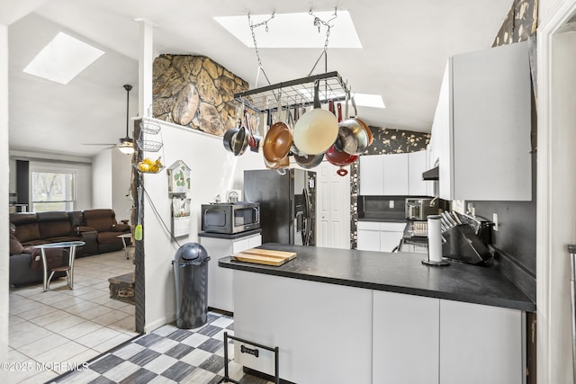kitchen with dark countertops, stainless steel microwave, a peninsula, lofted ceiling with skylight, and black refrigerator with ice dispenser