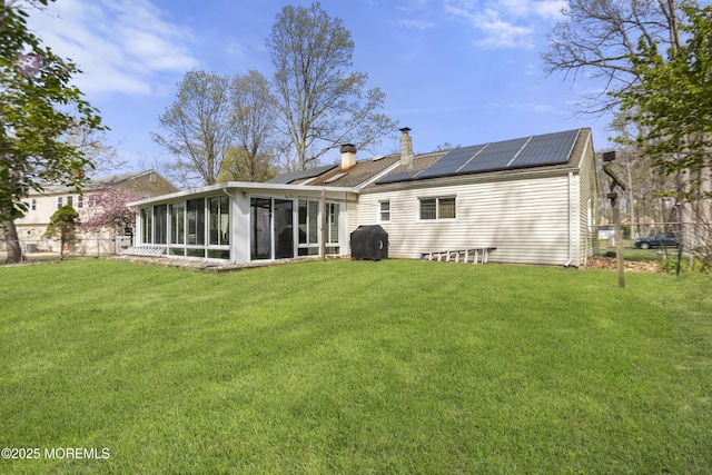back of house featuring a yard, a chimney, a sunroom, and solar panels