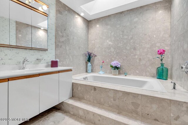 bathroom with vanity, a bath, a skylight, and tile walls
