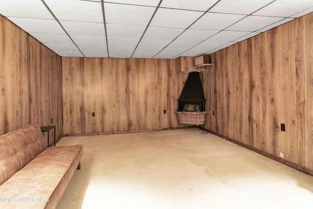 unfurnished living room featuring wood walls, concrete floors, a paneled ceiling, and a wood stove