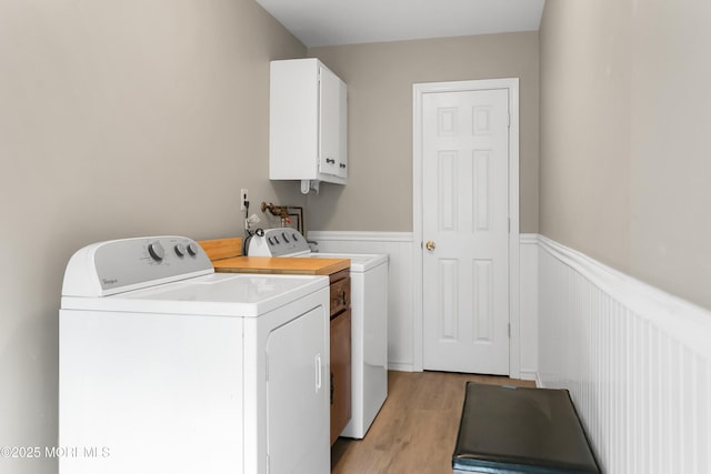 laundry room featuring cabinet space, wainscoting, washing machine and dryer, and light wood finished floors