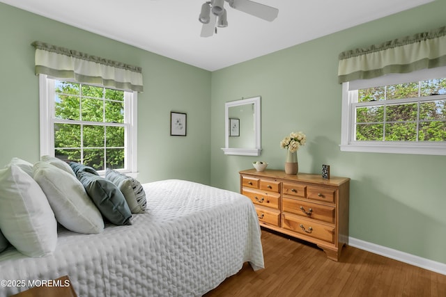 bedroom featuring baseboards, multiple windows, a ceiling fan, and wood finished floors