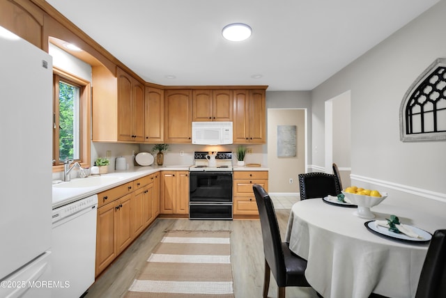 kitchen with a sink, light countertops, light wood-type flooring, and white appliances