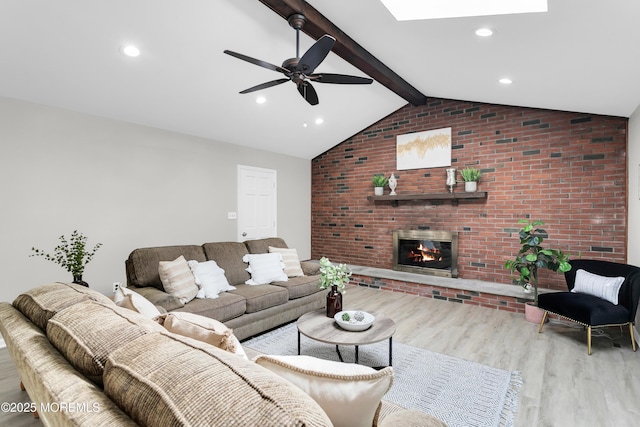 living area featuring a brick fireplace, brick wall, a ceiling fan, wood finished floors, and lofted ceiling with skylight