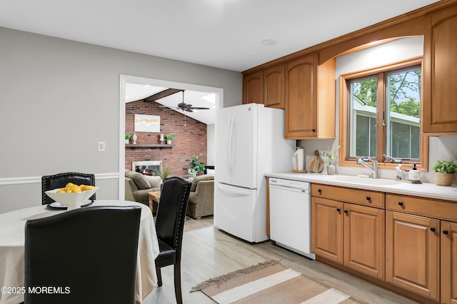 kitchen with lofted ceiling, brick wall, white appliances, a sink, and light wood-style flooring