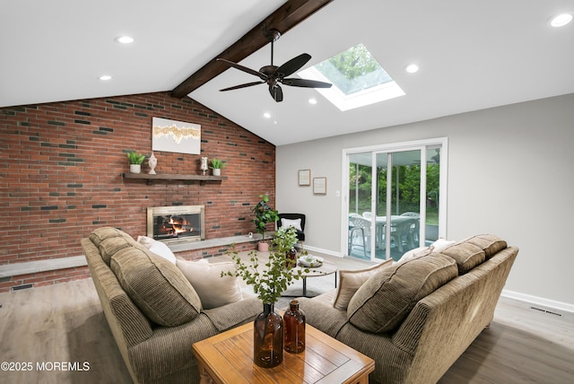 living area with vaulted ceiling with skylight, ceiling fan, brick wall, visible vents, and a fireplace