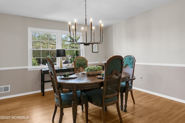 dining space with visible vents, baseboards, wood finished floors, and a notable chandelier