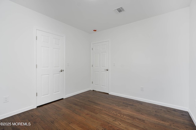 empty room with baseboards, visible vents, and dark wood-type flooring