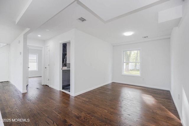 empty room featuring baseboards, visible vents, a wealth of natural light, and dark wood-style flooring