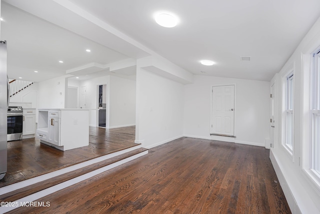 unfurnished living room with dark wood-style floors, baseboards, visible vents, and lofted ceiling