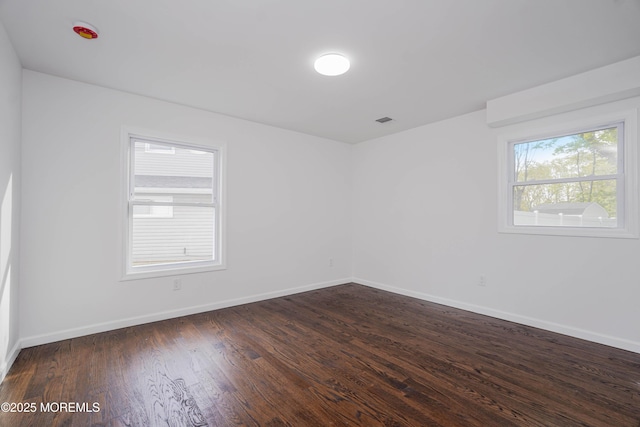 empty room with baseboards, visible vents, and dark wood finished floors