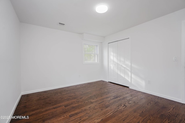 unfurnished bedroom featuring a closet, visible vents, wood finished floors, and baseboards