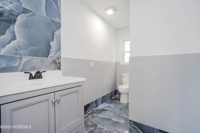 bathroom featuring tile walls, vanity, toilet, a wainscoted wall, and marble finish floor