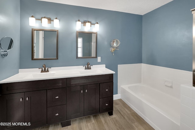 full bath featuring double vanity, a sink, a bath, and wood finished floors
