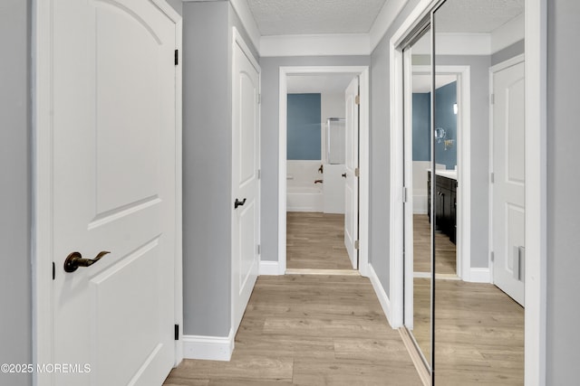 hall with baseboards, a textured ceiling, ornamental molding, and light wood-style flooring