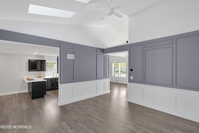 unfurnished living room with visible vents, wood finished floors, a decorative wall, ceiling fan, and vaulted ceiling with skylight