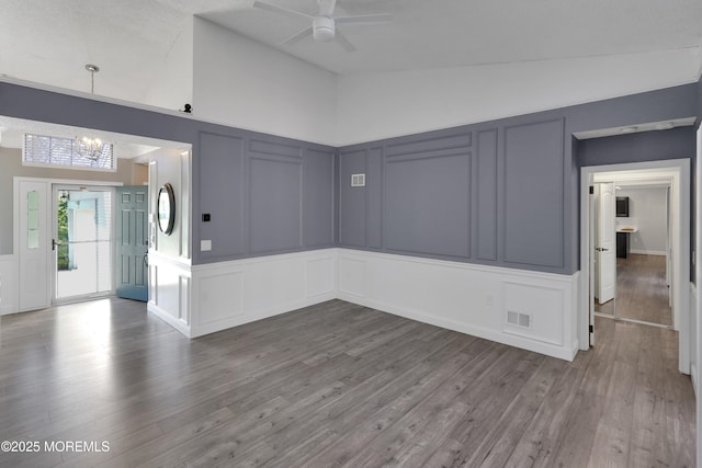 unfurnished room with vaulted ceiling, wood finished floors, ceiling fan with notable chandelier, and a decorative wall