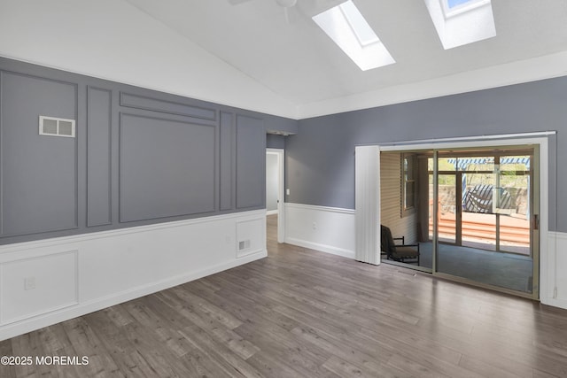 unfurnished room featuring a wainscoted wall, lofted ceiling with skylight, wood finished floors, and visible vents