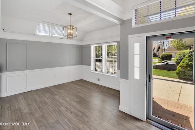 entryway featuring a decorative wall, vaulted ceiling, wood finished floors, and a notable chandelier