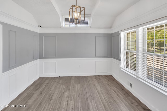 unfurnished dining area featuring an inviting chandelier, lofted ceiling, a decorative wall, and visible vents
