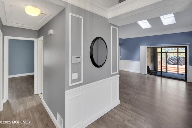 hall featuring a skylight, visible vents, wainscoting, and wood finished floors