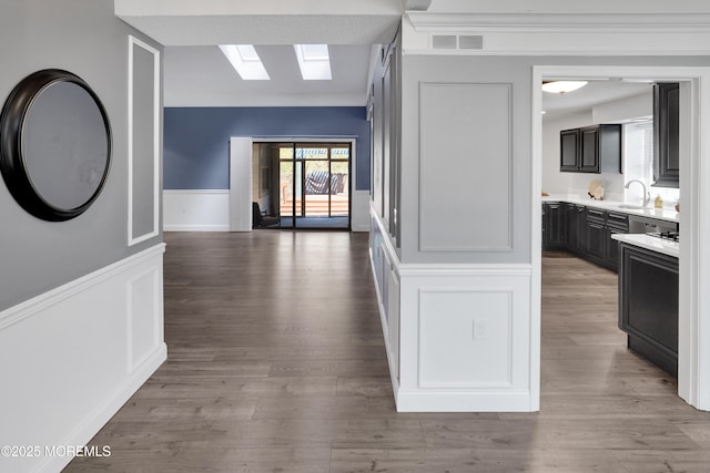 corridor featuring a skylight, visible vents, wainscoting, and a decorative wall
