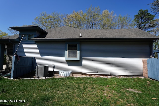 back of house with central AC unit, roof with shingles, and a yard