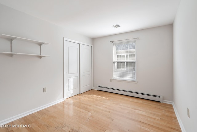 unfurnished bedroom with baseboards, wood finished floors, a baseboard radiator, visible vents, and a closet