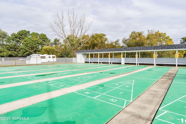 view of community with fence, a shed, an outdoor structure, and shuffleboard