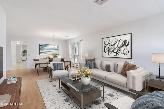 living area with visible vents, baseboard heating, wood finished floors, baseboards, and an inviting chandelier