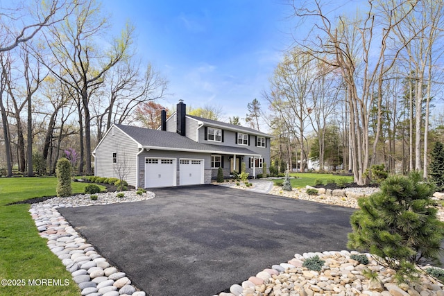 view of front facade featuring aphalt driveway, a chimney, a front lawn, and a garage