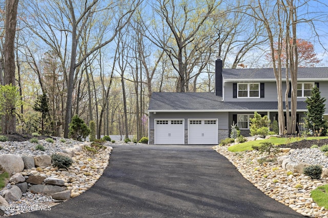 view of front of house featuring aphalt driveway, a chimney, stone siding, and a garage