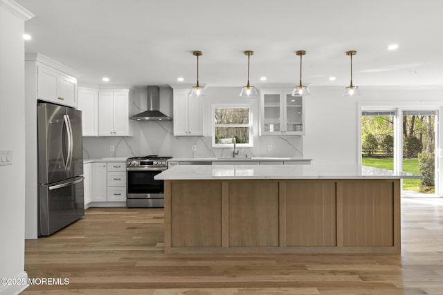 kitchen with wall chimney range hood, appliances with stainless steel finishes, a kitchen island, and recessed lighting
