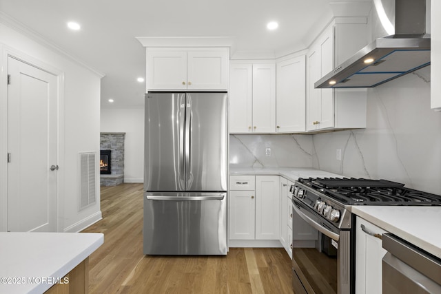 kitchen featuring wall chimney range hood, visible vents, light countertops, stainless steel appliances, and light wood-style flooring