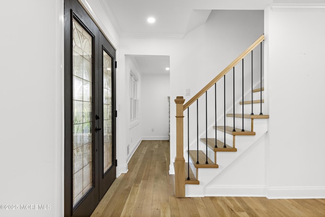 entryway featuring french doors, light wood-style flooring, baseboards, ornamental molding, and stairway