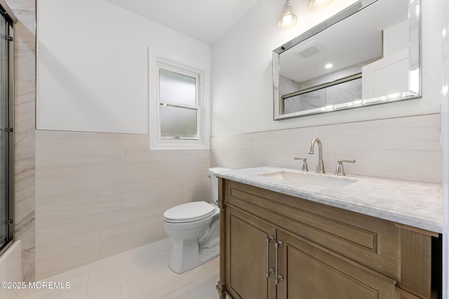 full bath featuring visible vents, tile walls, wainscoting, vanity, and toilet