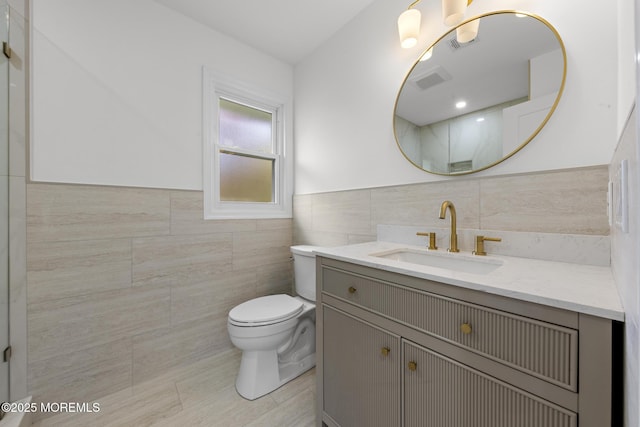 bathroom featuring vanity, wainscoting, toilet, and tile walls