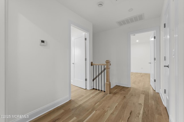hall featuring visible vents, baseboards, an upstairs landing, and light wood-type flooring