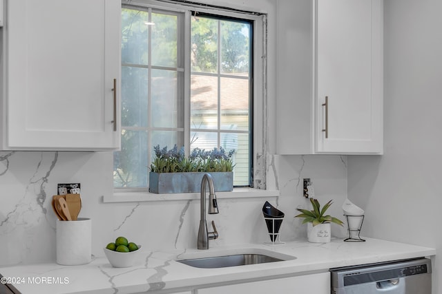 kitchen featuring stainless steel dishwasher, a sink, white cabinets, and backsplash