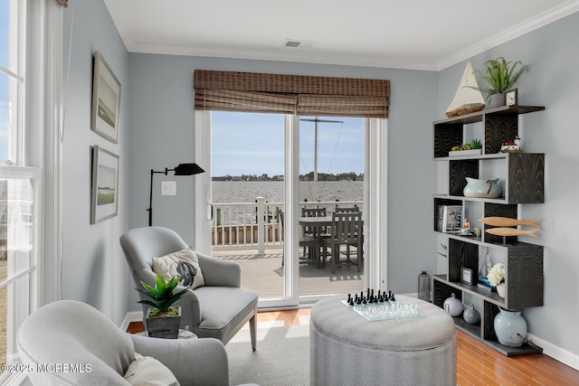 living area with baseboards, visible vents, ornamental molding, and wood finished floors