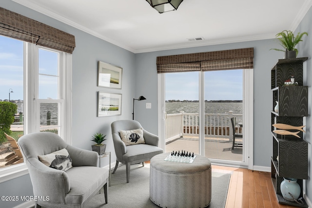 living area featuring crown molding, visible vents, a wealth of natural light, and light wood-style floors