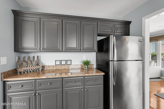 kitchen featuring gray cabinets, freestanding refrigerator, wood finished floors, and light stone countertops