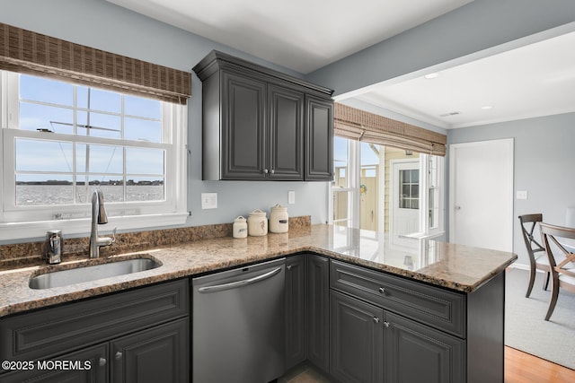 kitchen with stainless steel dishwasher, a peninsula, a sink, stone counters, and light wood finished floors