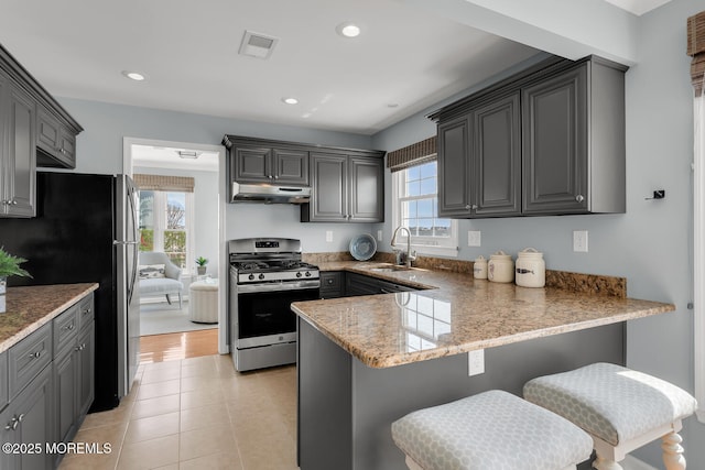 kitchen featuring a sink, stainless steel appliances, a peninsula, under cabinet range hood, and visible vents
