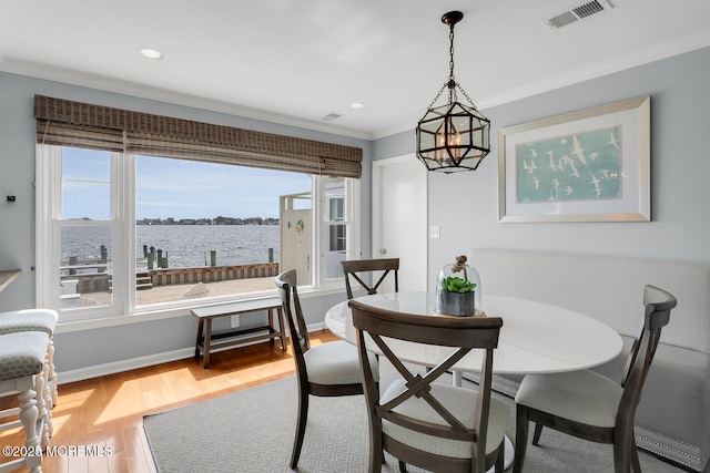 dining area featuring visible vents, crown molding, an inviting chandelier, wood finished floors, and a water view