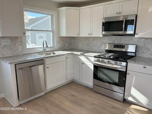 kitchen featuring light stone counters, white cabinets, a sink, stainless steel appliances, and light wood finished floors