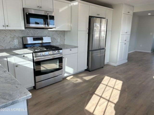 kitchen with wood finished floors, appliances with stainless steel finishes, white cabinets, backsplash, and baseboards