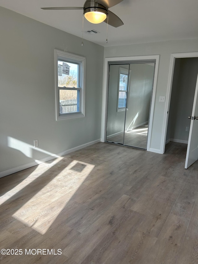 unfurnished bedroom with baseboards, visible vents, wood finished floors, and a closet