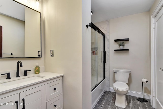 full bathroom featuring combined bath / shower with glass door, toilet, vanity, baseboards, and wood tiled floor