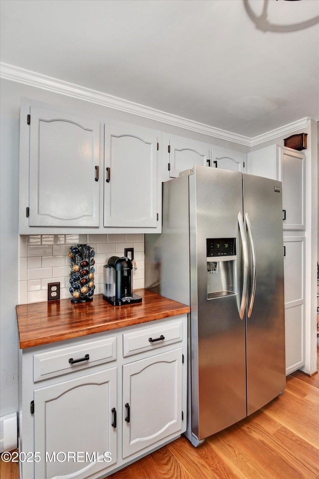 kitchen with wood counters, crown molding, light wood-style flooring, stainless steel fridge, and backsplash